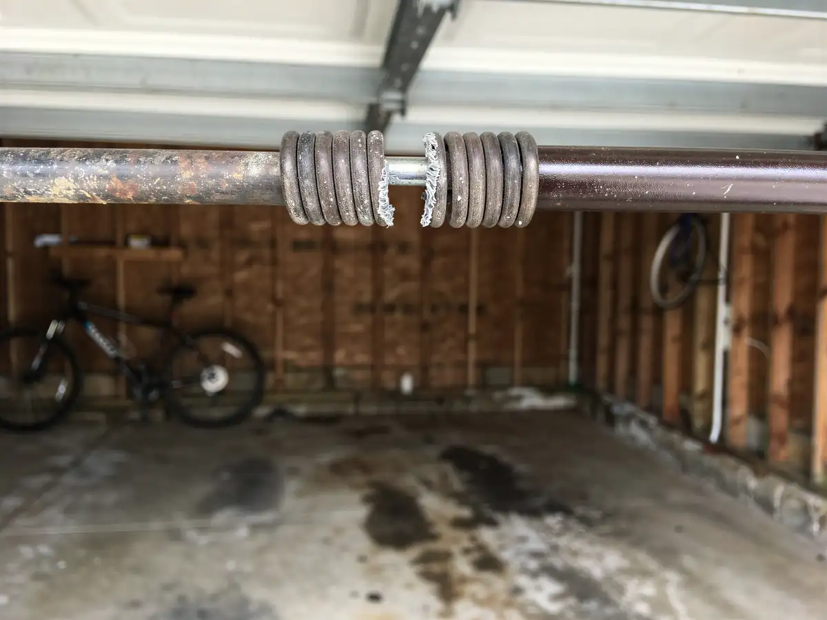 A broken torsion spring is visible on a garage door shaft.